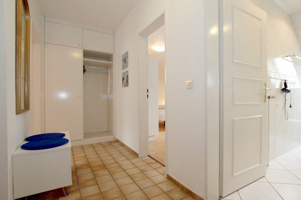Un couloir avec une porte blanche, un paillasson bleu et un sol carrelé.