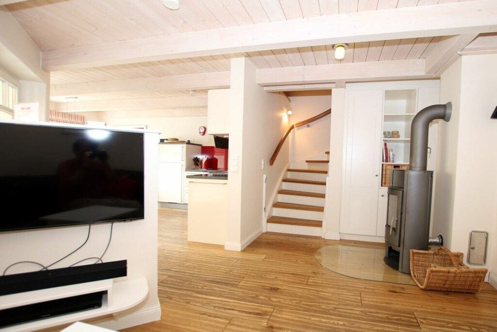 Un espace de vie moderne doté d’un téléviseur à écran plat, de planchers en bois, d’un coin cuisine et d’un escalier.
