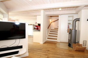A modern living space with a flat-screen TV, wooden flooring, a kitchen area, and a staircase. - Brandgans at Susanne-Fischer Weg 43 (Wyk auf Föhr)