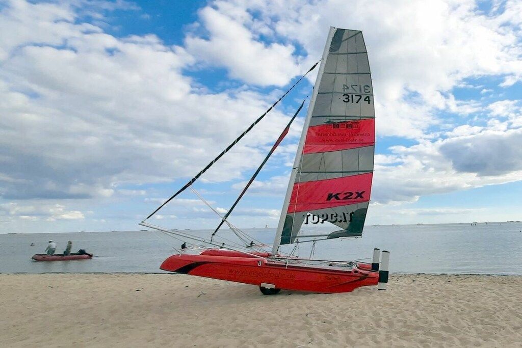 A sailboat with a red hull and a sail marked with 'K2X' and '3174' on a sandy beach.