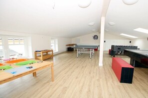 A spacious room with a foosball table, a long table with colorful mats, and a window with a view. - Brandgans at Susanne-Fischer Weg 43 (Wyk auf Föhr)