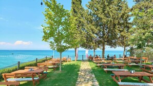 An outdoor seating area with wooden tables and benches, a stone pathway, and a view of the sea. - Hydros Beach Resort (Kemer)