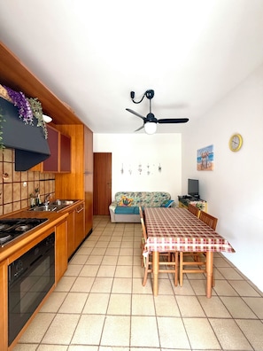 A compact kitchen with a dining area, wooden cabinets, a stove, and a ceiling fan. - Vacation rental sleeping 5 or 6 in the center of Marina di Ragusa. (Marina di Ragusa)