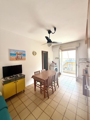 A dining area with a table and chairs, a television on a cabinet, and a ceiling fan. - Vacation rental sleeping 5 or 6 in the center of Marina di Ragusa. (Marina di Ragusa)