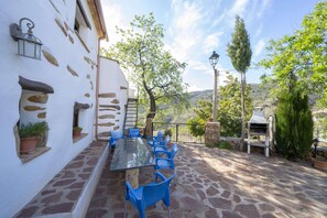 An outdoor patio with a glass table and blue chairs, stone walls, and a view of the countryside. - 6-guest Holiday Home in Central Laroya (Laroya)