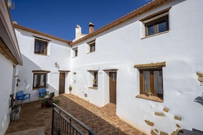 A courtyard with white walls, stone flooring, and wooden doors. There are potted plants and a blue chair. - 6-guest Holiday Home in Central Laroya (Laroya)