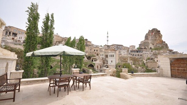 Un espacio al aire libre con mesa y sillas, con vistas a un pueblo histórico de arquitectura tradicional y una formación rocosa destacada.