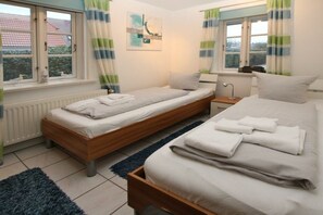 Ein Schlafzimmer mit zwei Betten, einem Fenster mit Vorhängen, einem Heizkörper und einem Gemälde an der Wand.