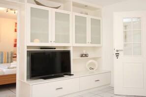 A hotel room with a television on a white cabinet, a bed with striped bedding, and a white door. - 2 - Rungholtstraße 3c (Wyk auf Föhr)
