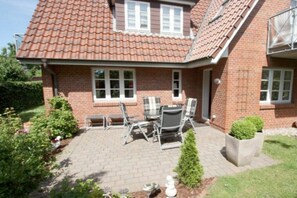 Ein zweistöckiges Ziegelhaus mit einem Ziegeldach, einer Terrasse mit Gartenmöbeln und einer kleinen Grünfläche.