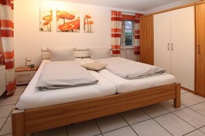 A bedroom with a wooden bed, white bedding, a nightstand, a lamp, and a wardrobe. - 2 - Rungholtstraße 3c (Wyk auf Föhr)