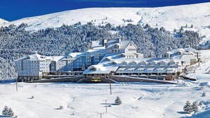 Et snedækket hotel med flere bygninger, en skibakke i baggrunden og en skovklædt bakke.