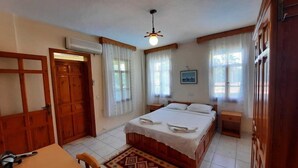 Un dormitorio con cama, escritorio y silla. Hay un ventilador de techo, una ventana con cortinas y un aire acondicionado de pared.