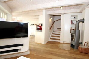 Una sala de estar moderna con una televisión de pantalla plana, piso de madera, una escalera y un estufa de leña.
