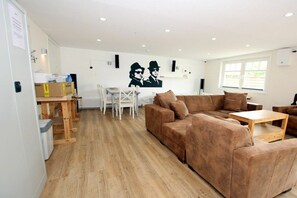 A modern living room with a brown sofa, a wooden coffee table, and a white dining table with chairs. There is a large window on the right and a wall with a black and white mural. - Seestern at Susanne-Fischer Weg 25 (Wyk auf Föhr)