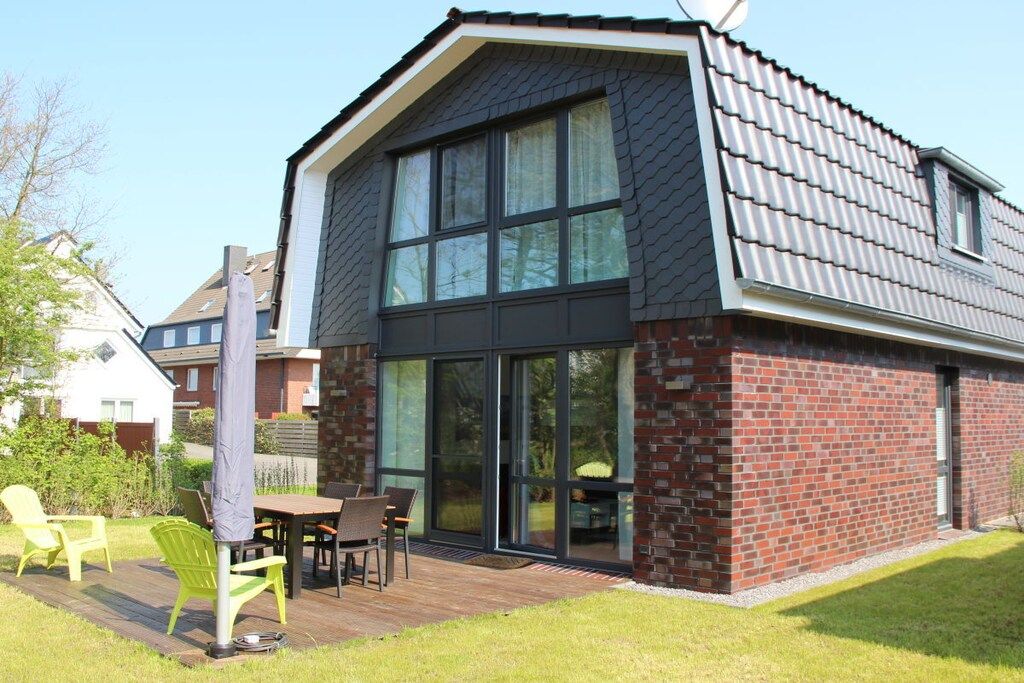 A modern house with a large glass door entrance, a deck with outdoor furniture, and a brick exterior.