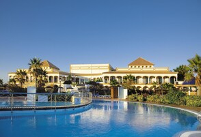 A resort with a large pool, palm trees, and Mediterranean-style architecture.