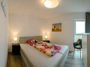A hotel room with a bed, two bedside lamps, a colorful blanket, a chair, a painting, and a window. - 49.6.n Dwarsloper (Wangerland)