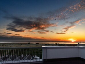 A sunset view from a balcony overlooking a beach with a fence in the foreground. - 49.6.n Dwarsloper (Wangerland)