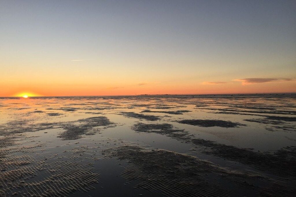 A beach at sunset with a calm sea and a clear sky.