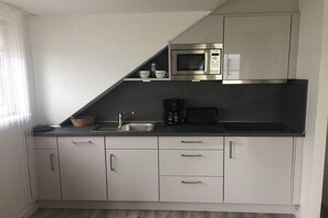 A modern kitchen with white cabinets, a microwave, a coffee maker, and a sink. - Holiday apartment with 1 bedroom (Cuxhaven)