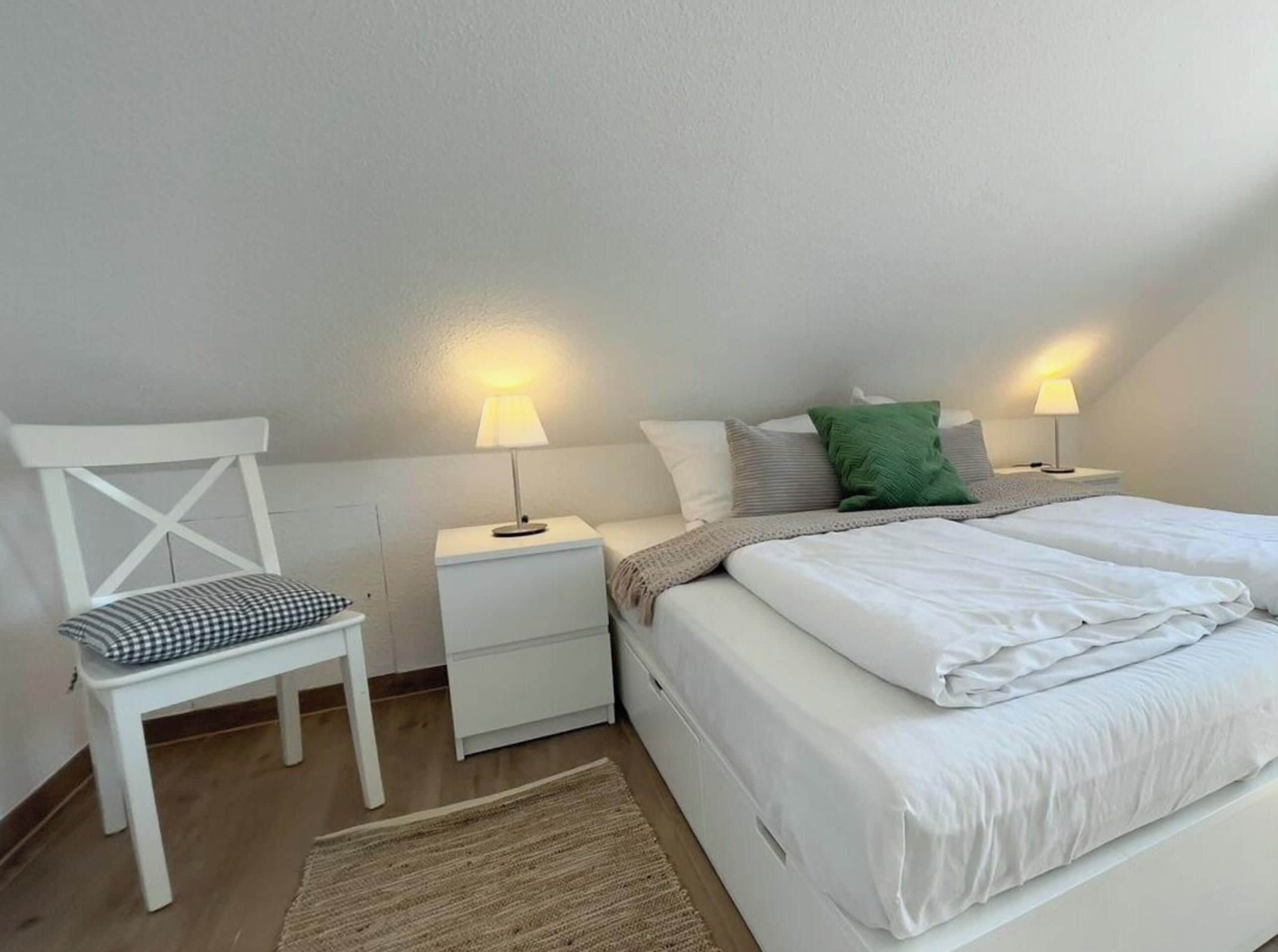 Un dormitorio con una cama, dos mesitas de noche con lámparas, una silla y una alfombra.