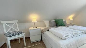 Un dormitorio con una cama, dos mesitas de noche con lámparas, una silla y una alfombra.