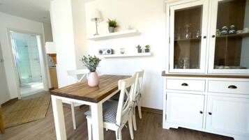 Un comedor con una mesa de madera y sillas blancas, un armario blanco con puertas de cristal y un pequeño estante con objetos decorativos.