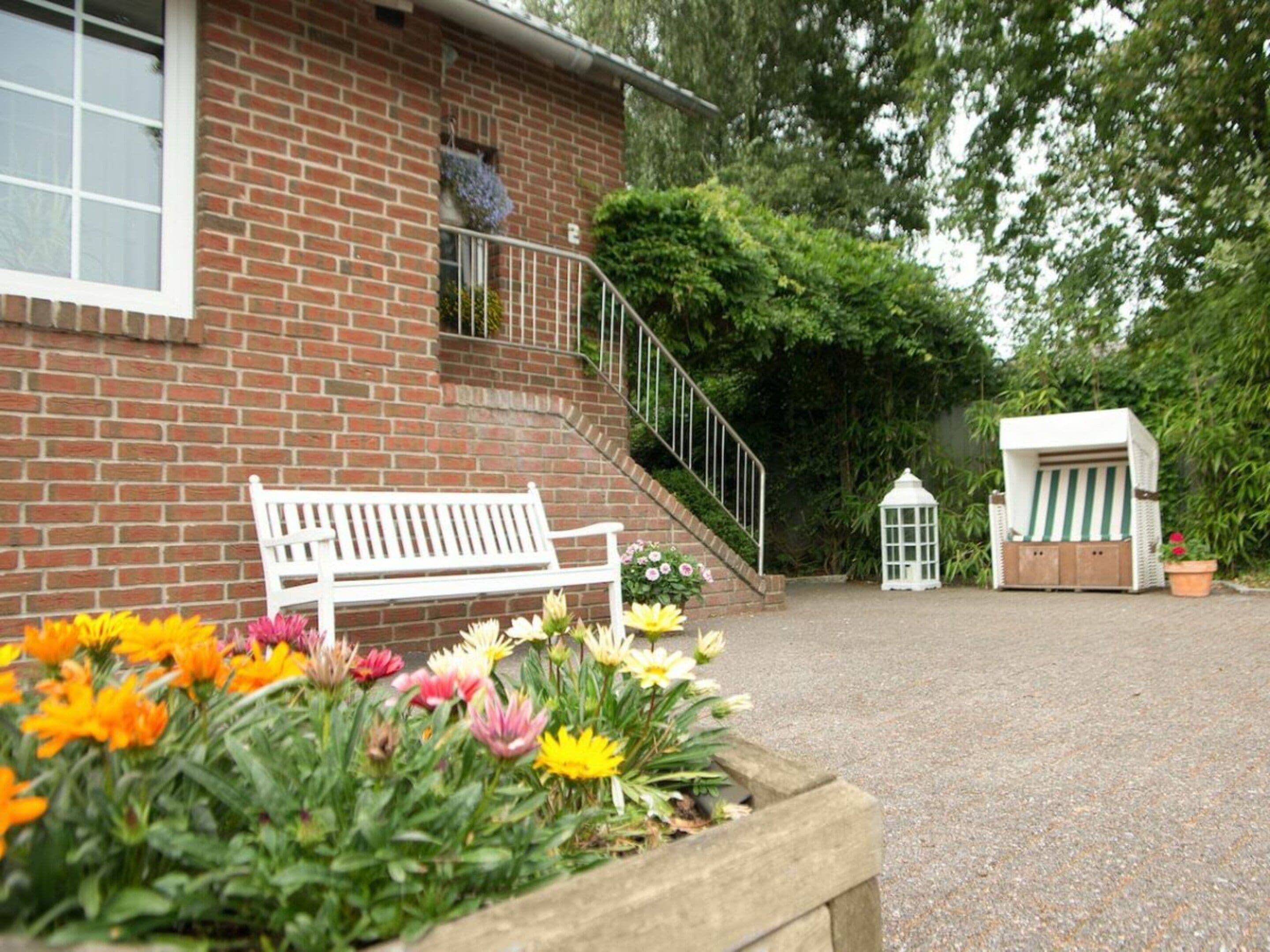 Un edificio de ladrillo con un banco blanco, una pequeña escalera y una jardinera con flores.