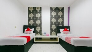 A room with two beds, a small table, and a patterned wall. - OYO 3428 Hotel Marimar (Palangkaraya)