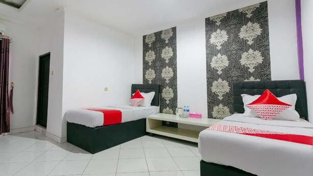 A hotel room with two beds, a small seating area, and a patterned wall. - OYO 3428 Hotel Marimar (Palangkaraya)