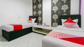 A hotel room with two beds, a small table, and a wall with a floral pattern. - OYO 3428 Hotel Marimar (Palangkaraya)