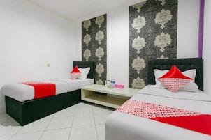 Una habitación de hotel con dos camas, una mesita pequeña y una pared con estampado floral.