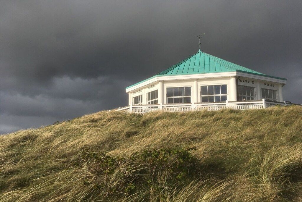 A white building with a green roof on a grassy hill, labeled 'MARIE HOME'.