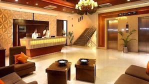 Een hotellobby met een receptiebalie, een zithoek en een lift.