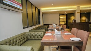 Een restaurant met een lange tafel, comfortabele zitmogelijkheden en een televisiescherm waarop nieuws te zien is.