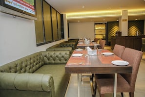 Un restaurant avec une longue table, des sièges confortables et un écran de télévision diffusant les actualités.