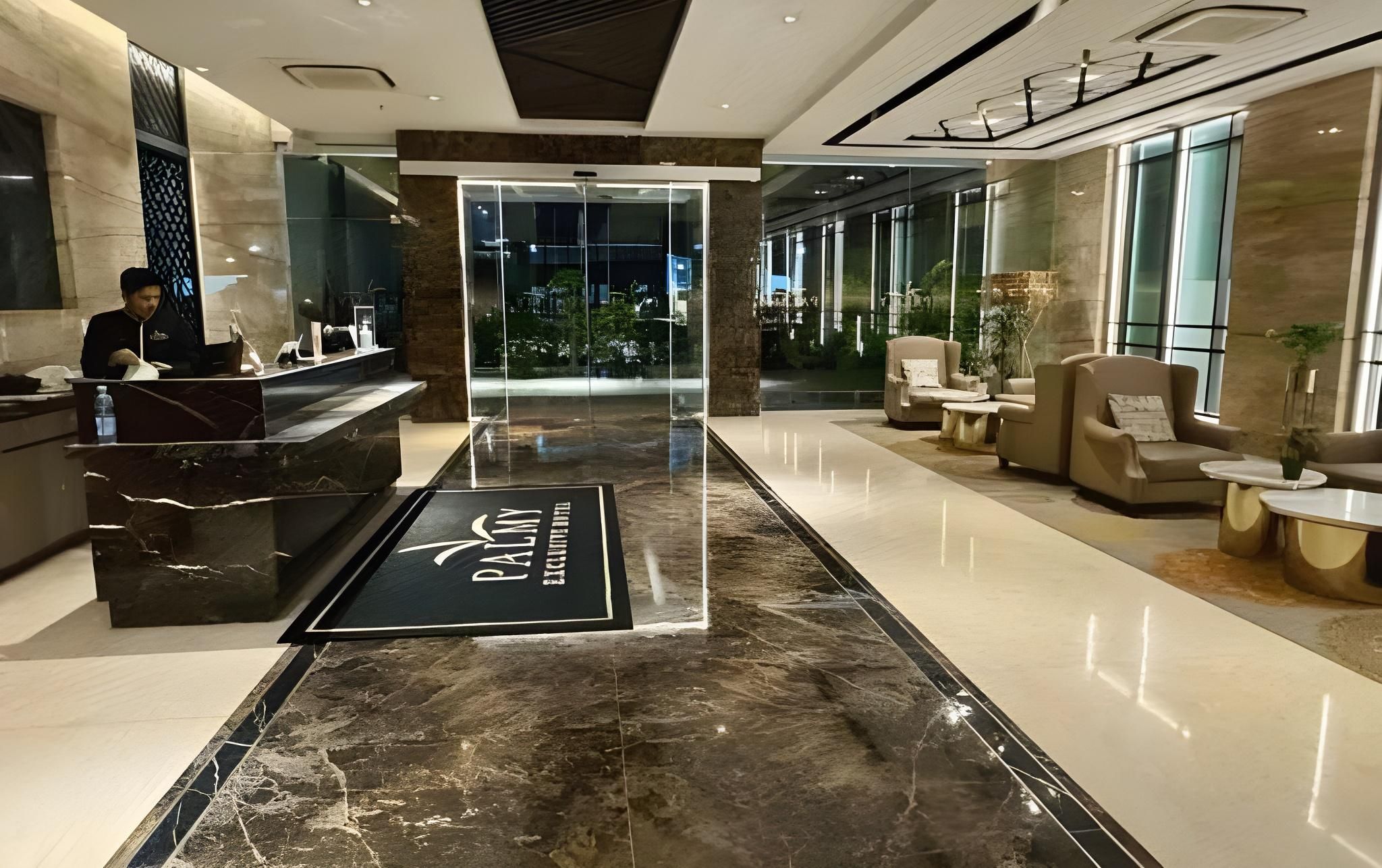 A hotel reception area with a marble floor, a reception desk, and seating area with armchairs and a coffee table.