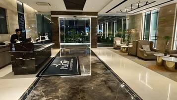 A hotel reception area with a marble floor, a reception desk, and seating area with armchairs and a coffee table.