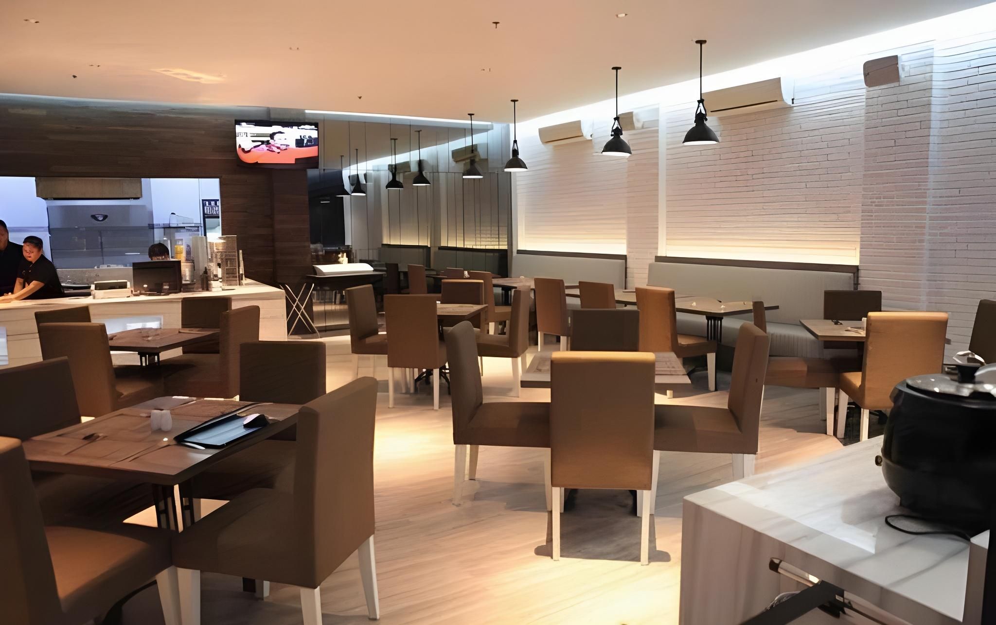 A modern restaurant interior with multiple tables and chairs, a television mounted on the wall, and pendant lighting.