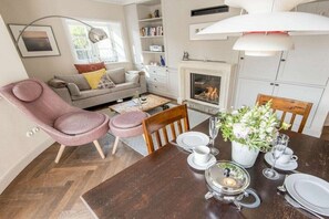 A dining area with a wooden table set for two, a fireplace, and a cozy seating arrangement with a sofa and armchairs. - Holiday apartment in Westerland with sauna (Westerland)