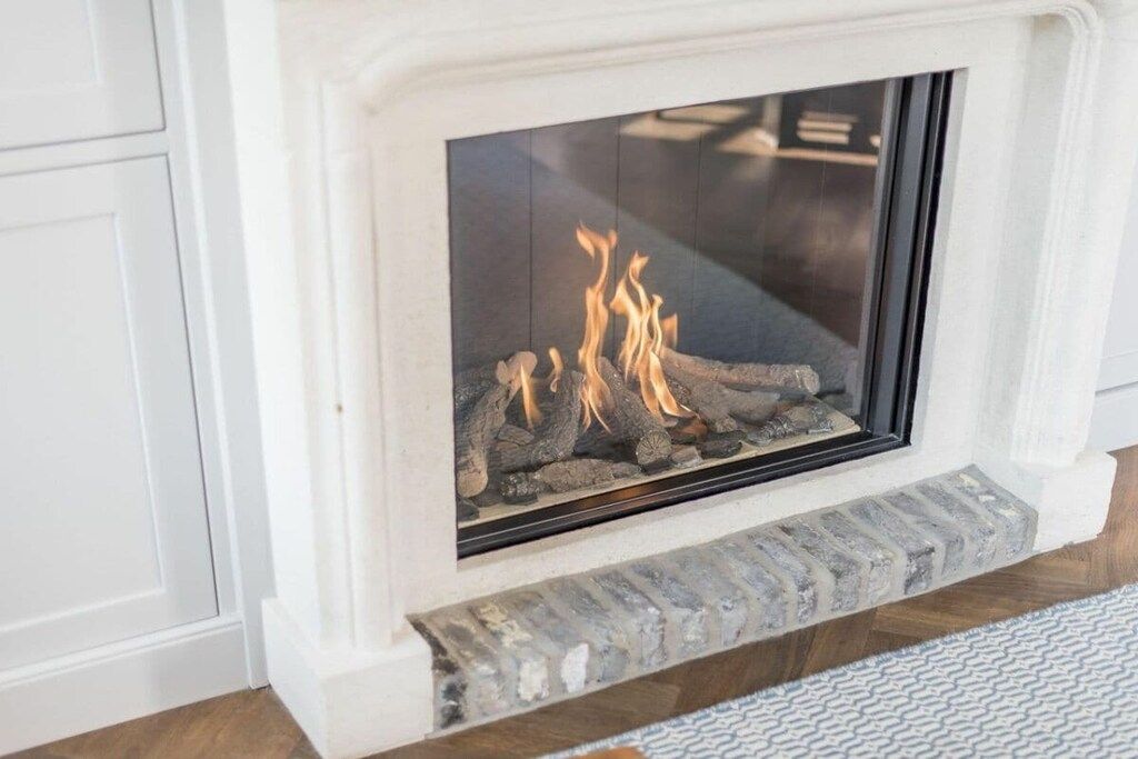A fireplace with a glass front, a stone base, and a white wall surrounding it.