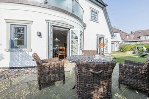 A white building with a curved exterior, a glass door entrance, wicker furniture, and a patio area. - Holiday apartment in Westerland with sauna (Westerland)