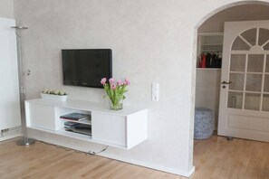 Eine weiße Unterhaltungsanlage mit einem Flachbildfernseher, einer Vase mit Blumen und einer kleinen Pflanze auf einem Regal.