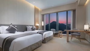 Ein Hotelzimmer mit zwei Betten, einem Schreibtisch, einem Stuhl und einem großen Fenster mit Blick.