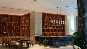 Eine moderne Lobby mit einer zentralen Sitzgruppe, einem großen Bücherregal aus Holz und einer Marmor-Theke.