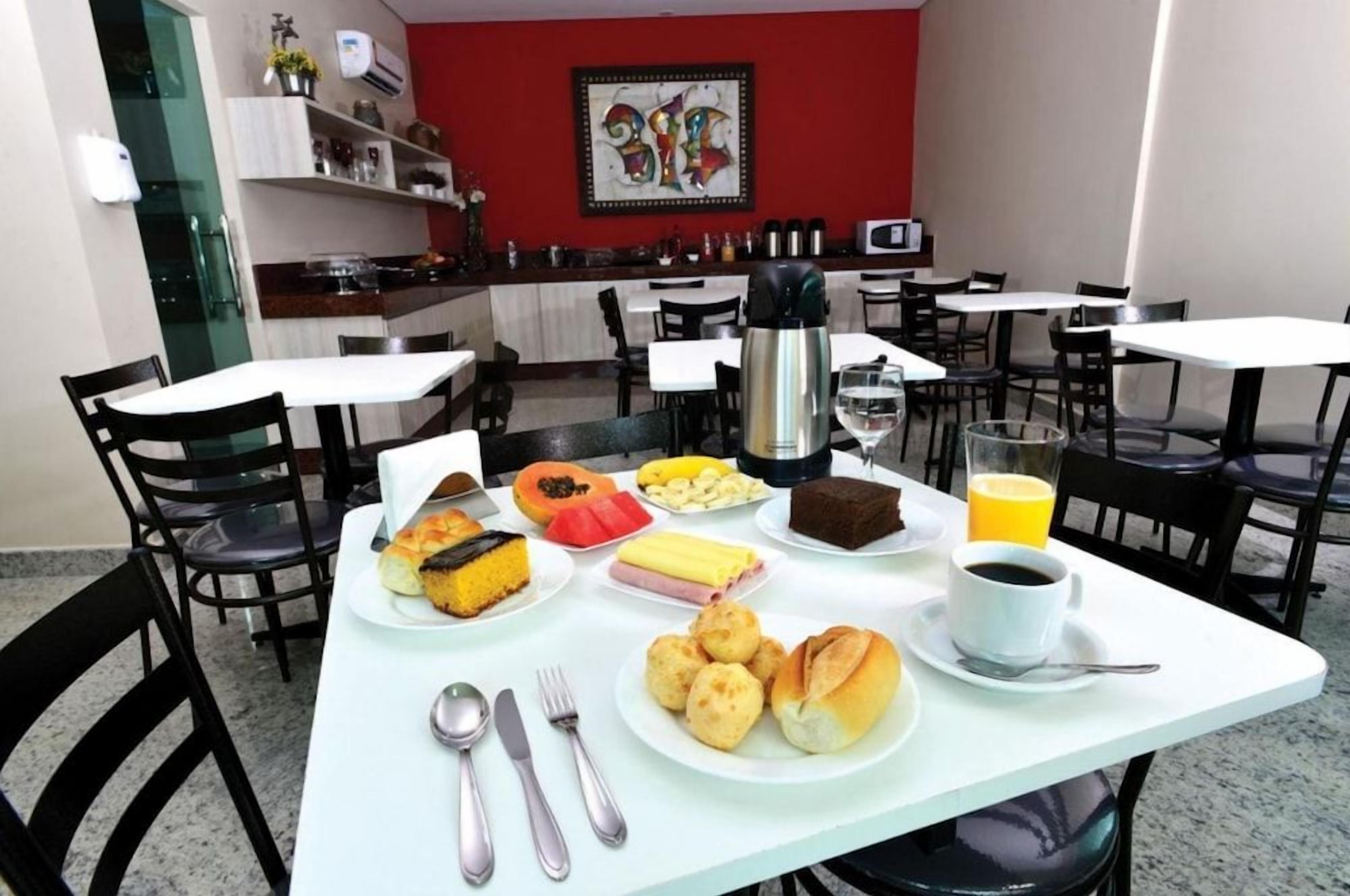 Uma área de refeições com mesas, cadeiras e diversos alimentos, incluindo pão, doces e uma bebida quente.