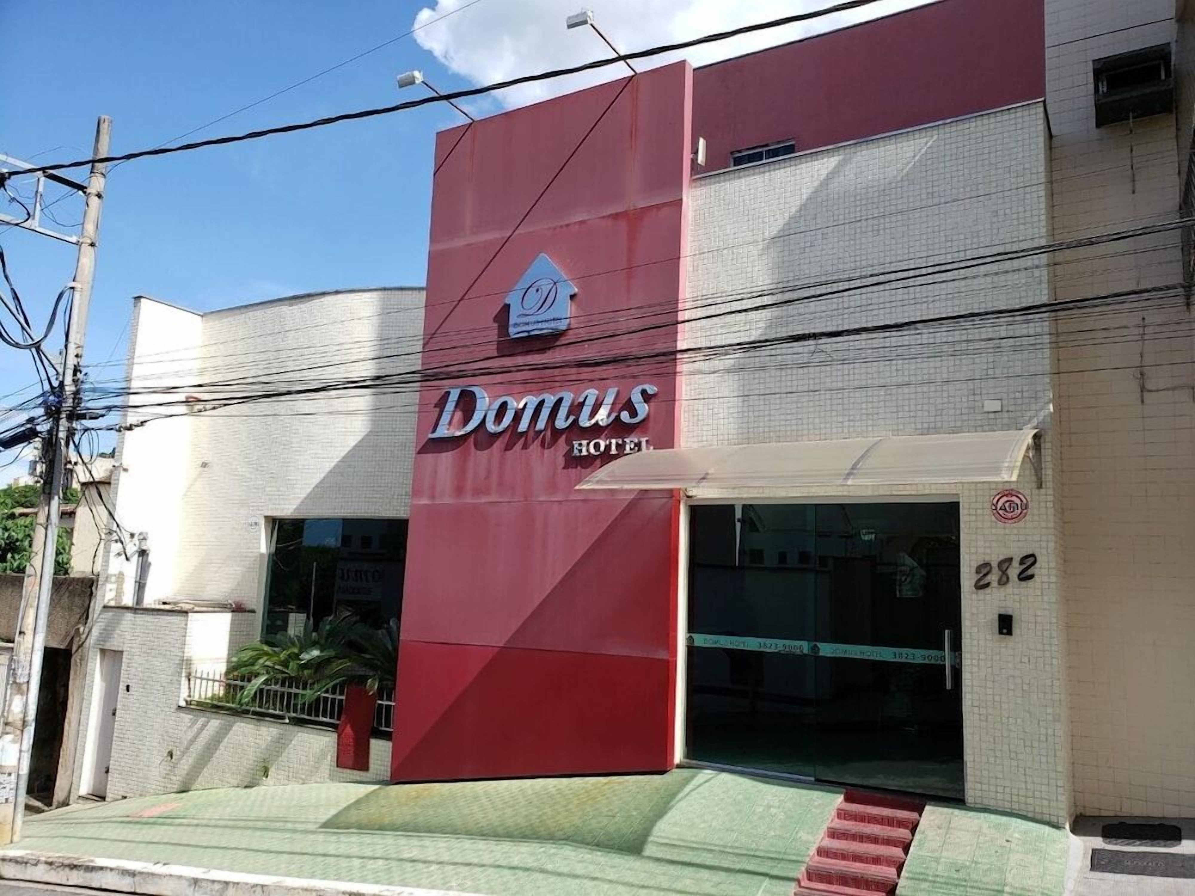 Um hotel chamado Domus, com fachada vermelha marcante e um amplo acesso por janela.