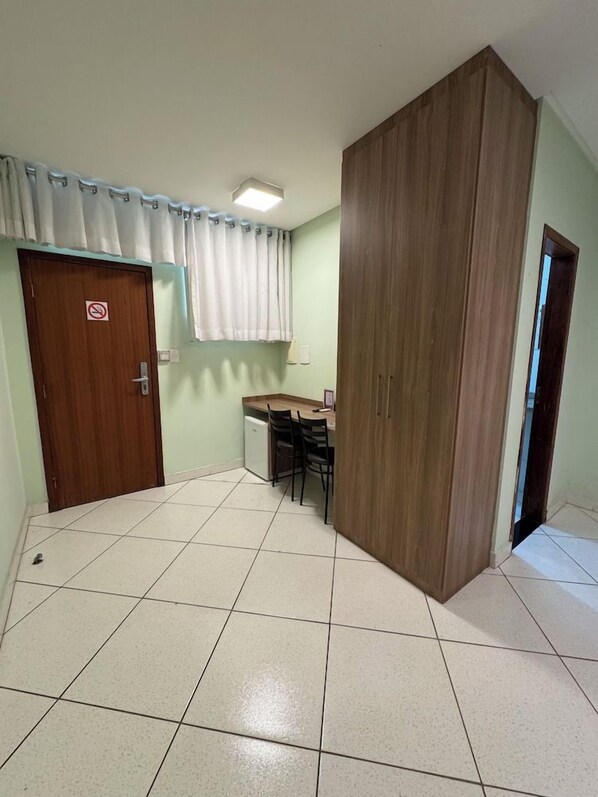 Una habitación con piso de baldosas, un armario de madera, un escritorio con sillas y una puerta con letrero de no fumar.