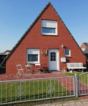Une maison en briques rouges avec une porte blanche, un petit porche doté d’un banc et une clôture blanche.